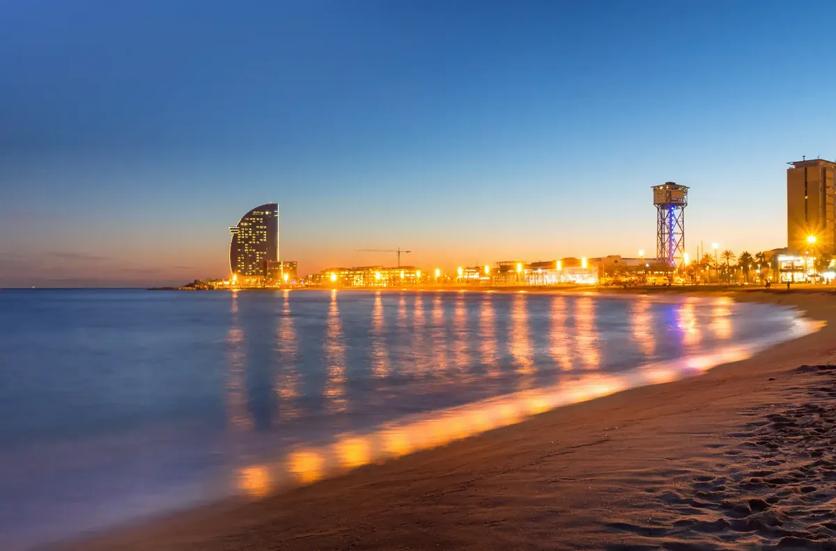 The Barceloneta beach at dusk with the seafront lights reflected in the calm sea