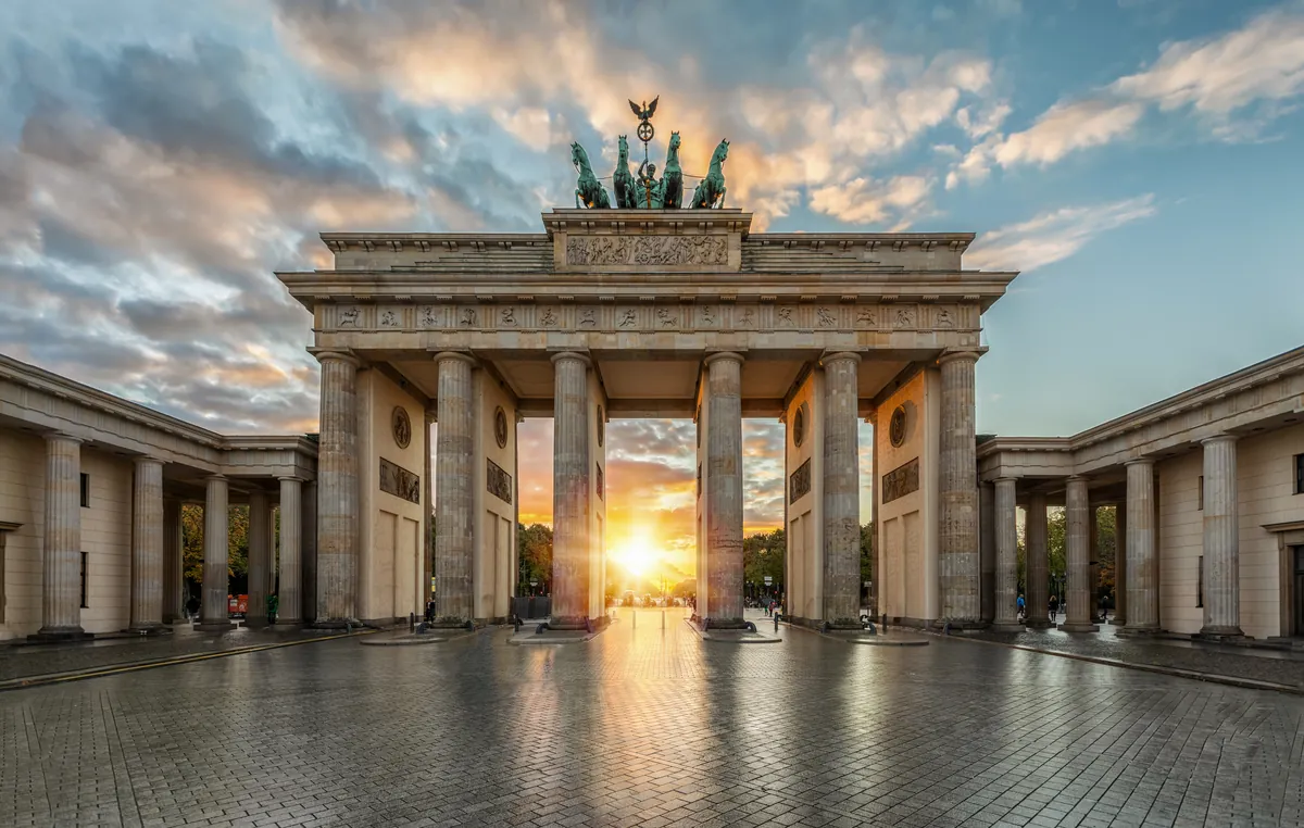 The Brandenburg Gate in Berlin with the low sun shining through its central columns across an empty cobbled square