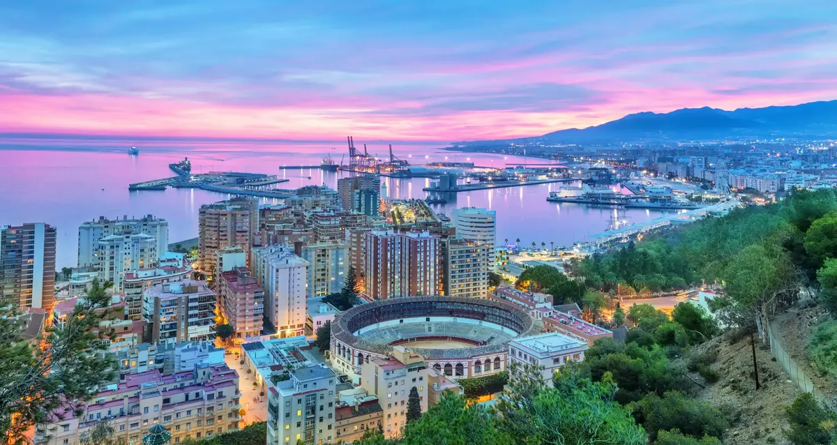 Málaga at dusk under a pink sky, the bullring, the port and the coast towards the east