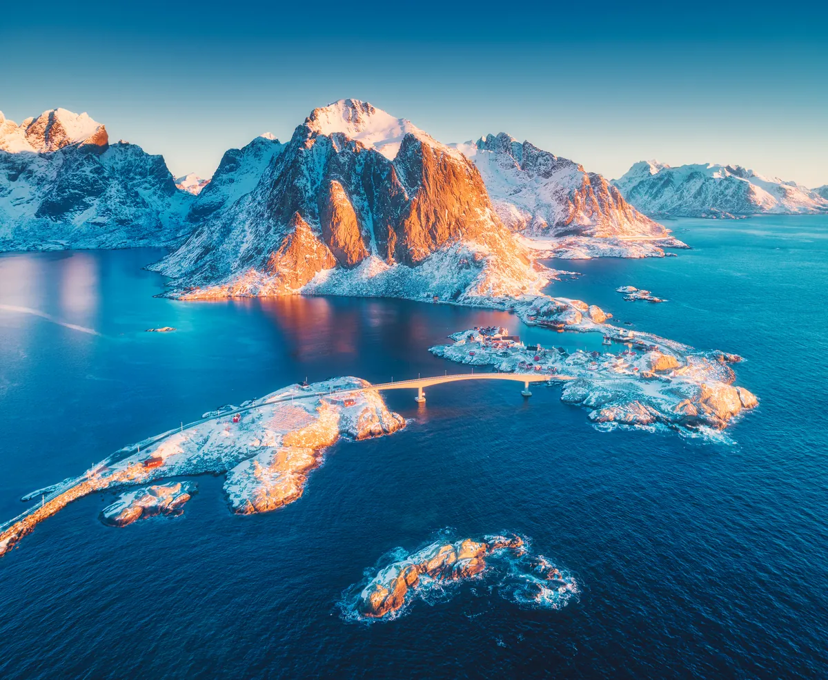 Aerial view of the Lofoten villages of Reine and Hamnøy at a winter sunrise, peaks glowing above the sea