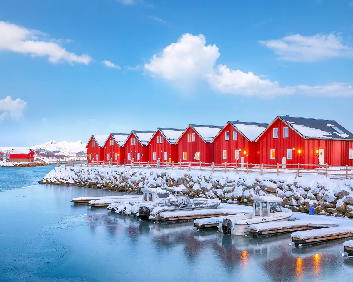 A row of red wooden fishermen’s cabins by the water on a snowy northern coast