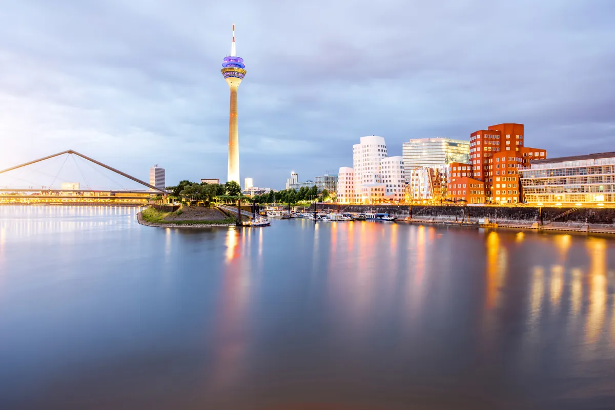 The Rheinturm and the curving Gehry buildings of the MedienHafen in Düsseldorf reflected in calm water at dusk
