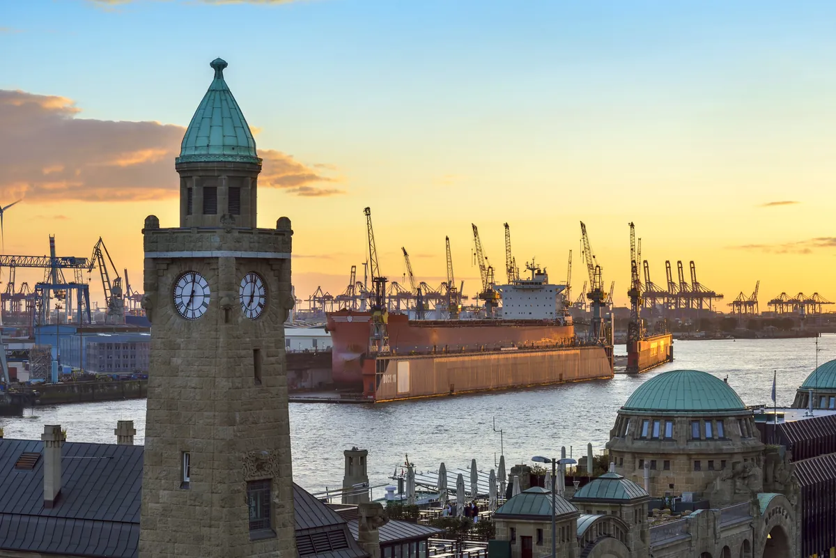 The clock tower of the St Pauli landing stages in Hamburg at sunset with harbour cranes behind