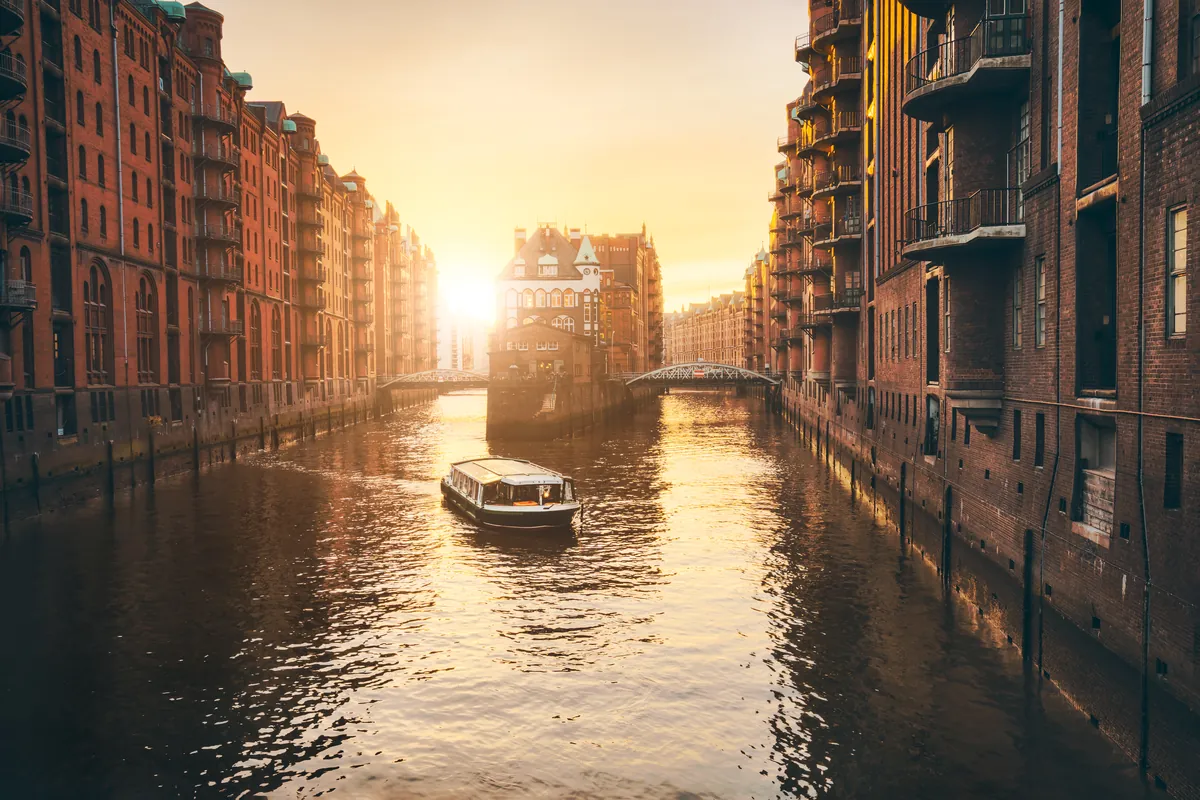 A canal between tall brick warehouses in Hamburg at golden hour, a small boat on the water