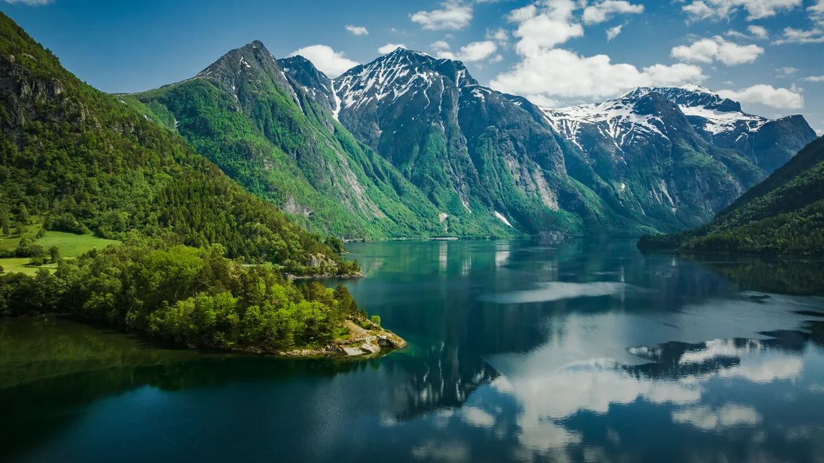 The still Eikesdalsvatnet lake in Norway reflecting steep green mountains and snowy peaks