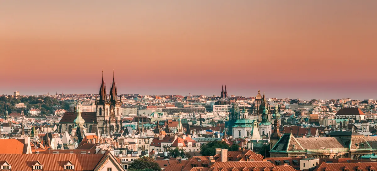 Prague’s Old Town rooftops at sunset with the twin Gothic spires of the Týn Church against a pink sky