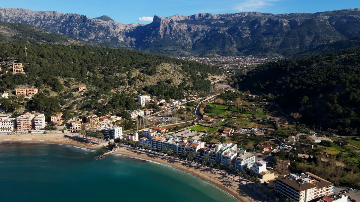 Aerial view of the curved bay of Port de Sóller with the Serra de Tramuntana and the town of Sóller in the valley behind