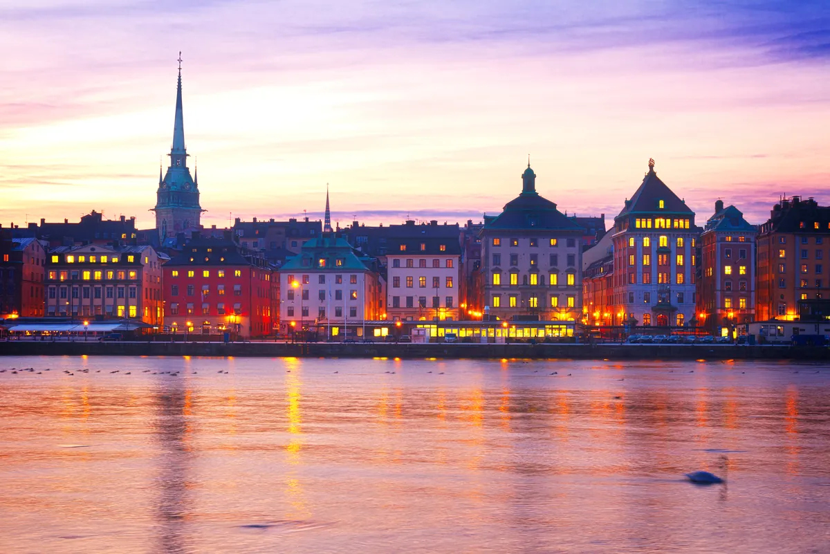 The old town of Stockholm under a pink and violet sky at dusk, lights reflected in the water
