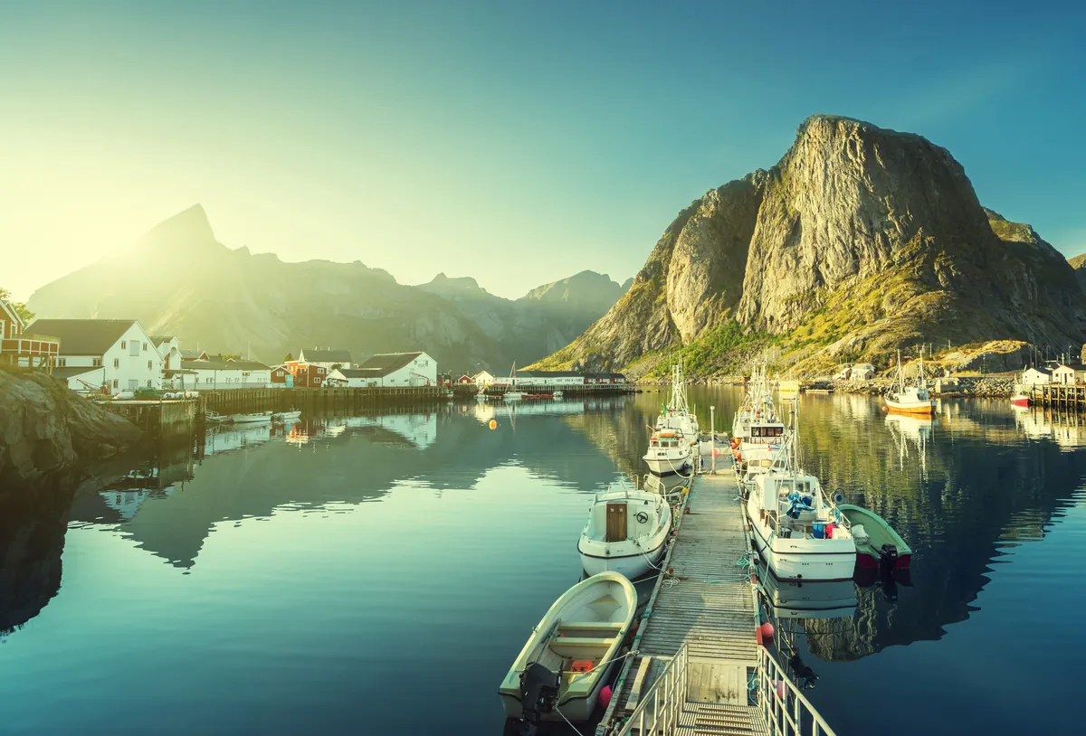 Boats moored at a wooden pier below steep green mountains on the Lofoten Islands in soft evening light