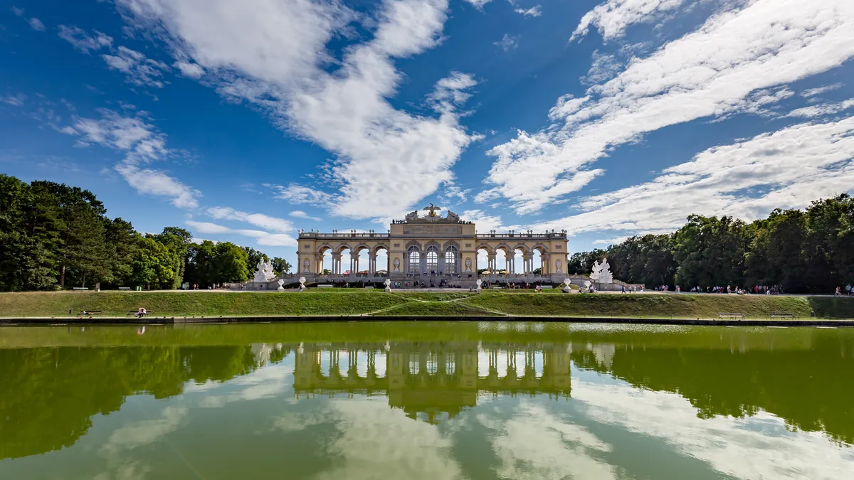 The Gloriette above the gardens of Schönbrunn Palace in Vienna reflected in a pond under a blue sky