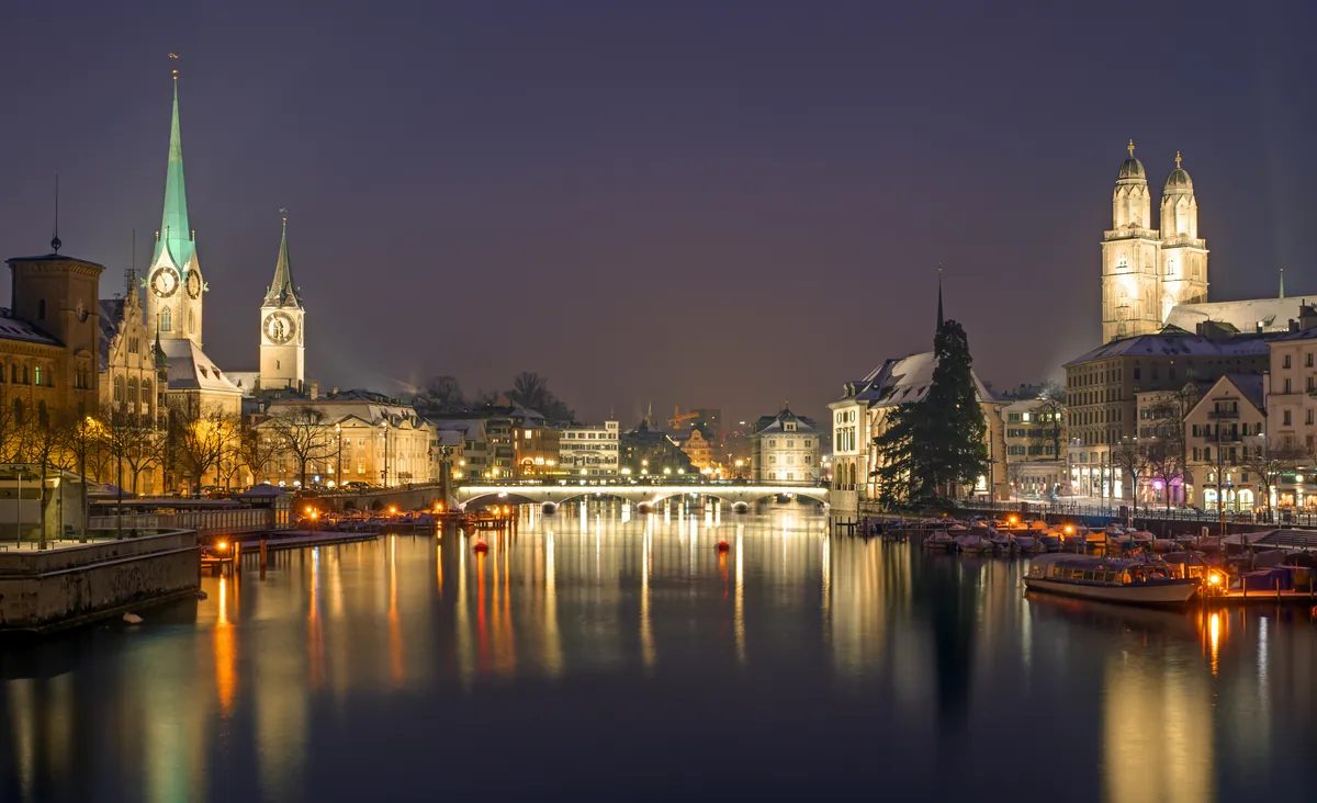 Zurich’s old town on the Limmat at night with the spires of St Peter and the Fraumünster and the twin towers of the Grossmünster